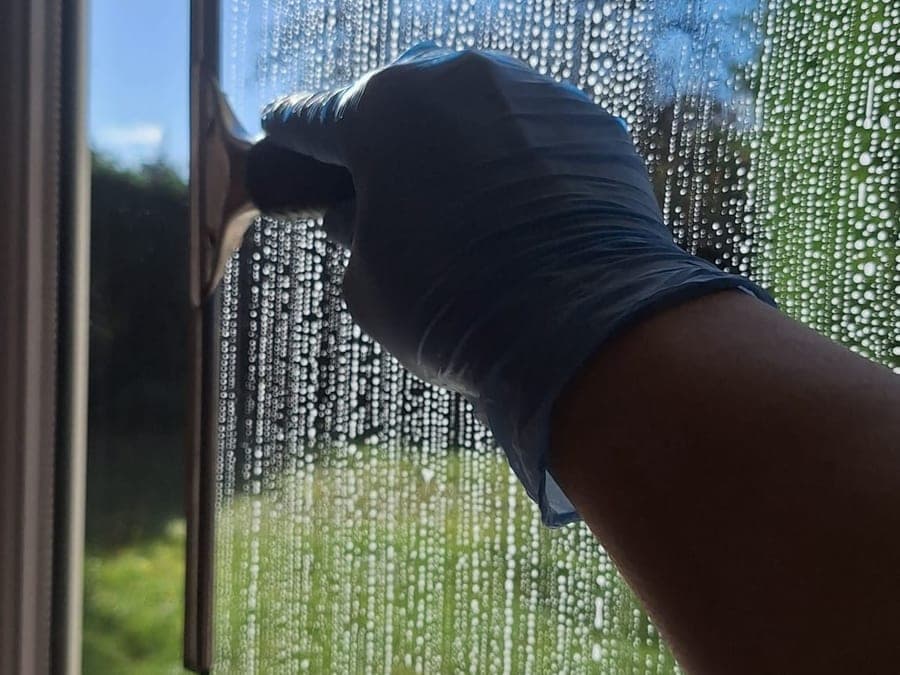 Main gantée de bleu et raclette sur une vitre ruisselante