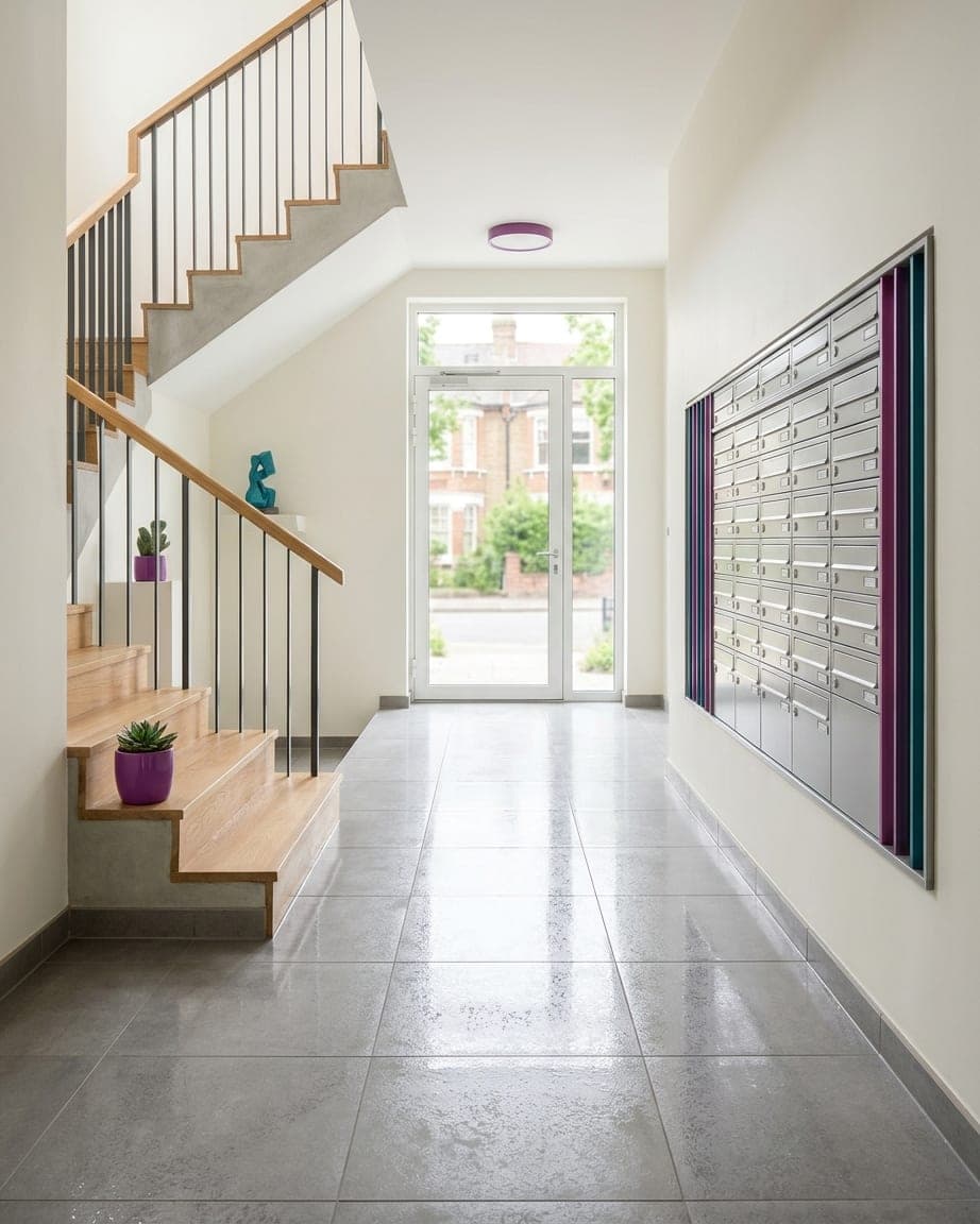 Hall d’immeuble au carrelage brillant, départ d’escalier et rangée de boîtes aux lettres