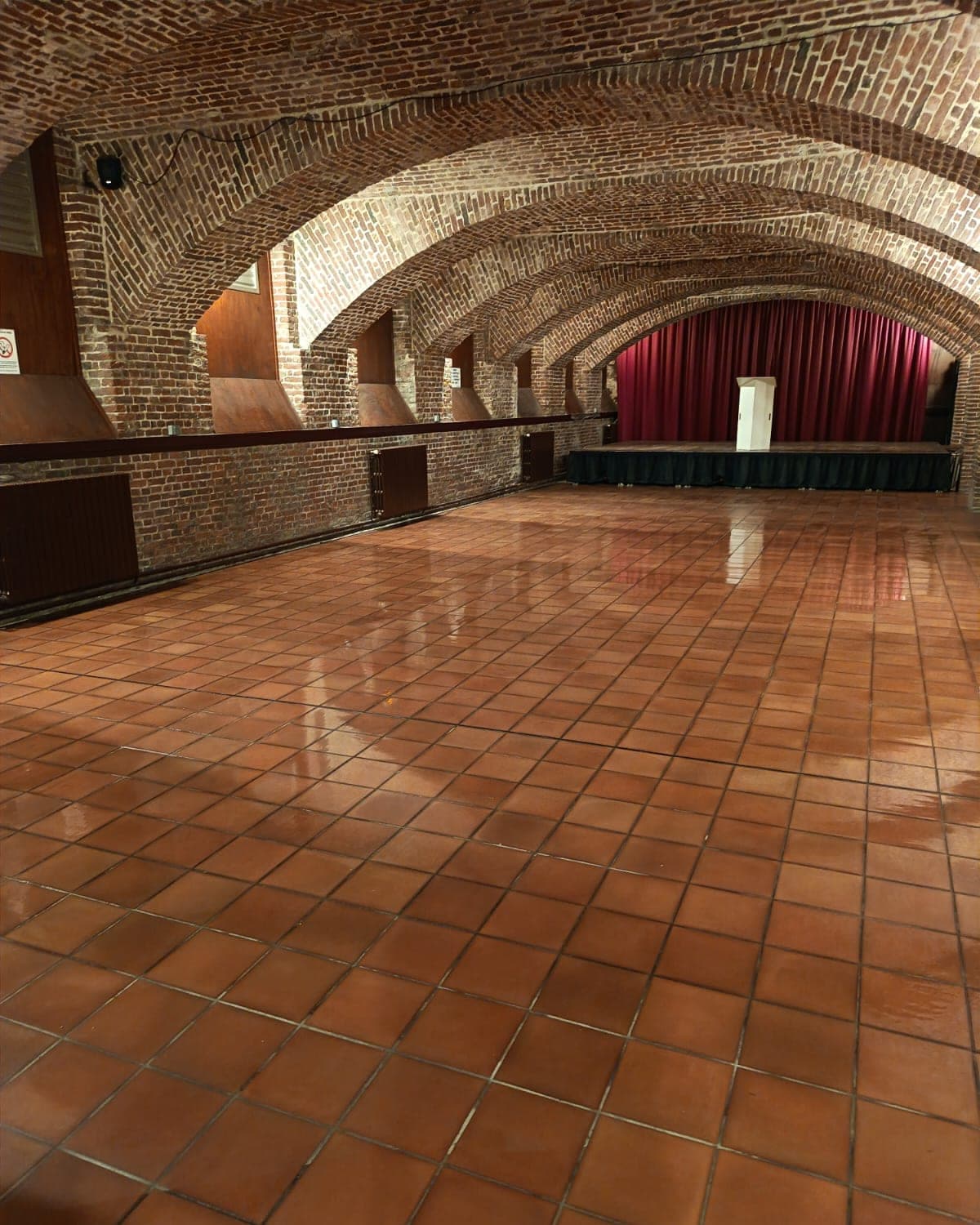 Grande salle voûtée en briques, scène au fond, sol en terre cuite lavé aux reflets brillants
