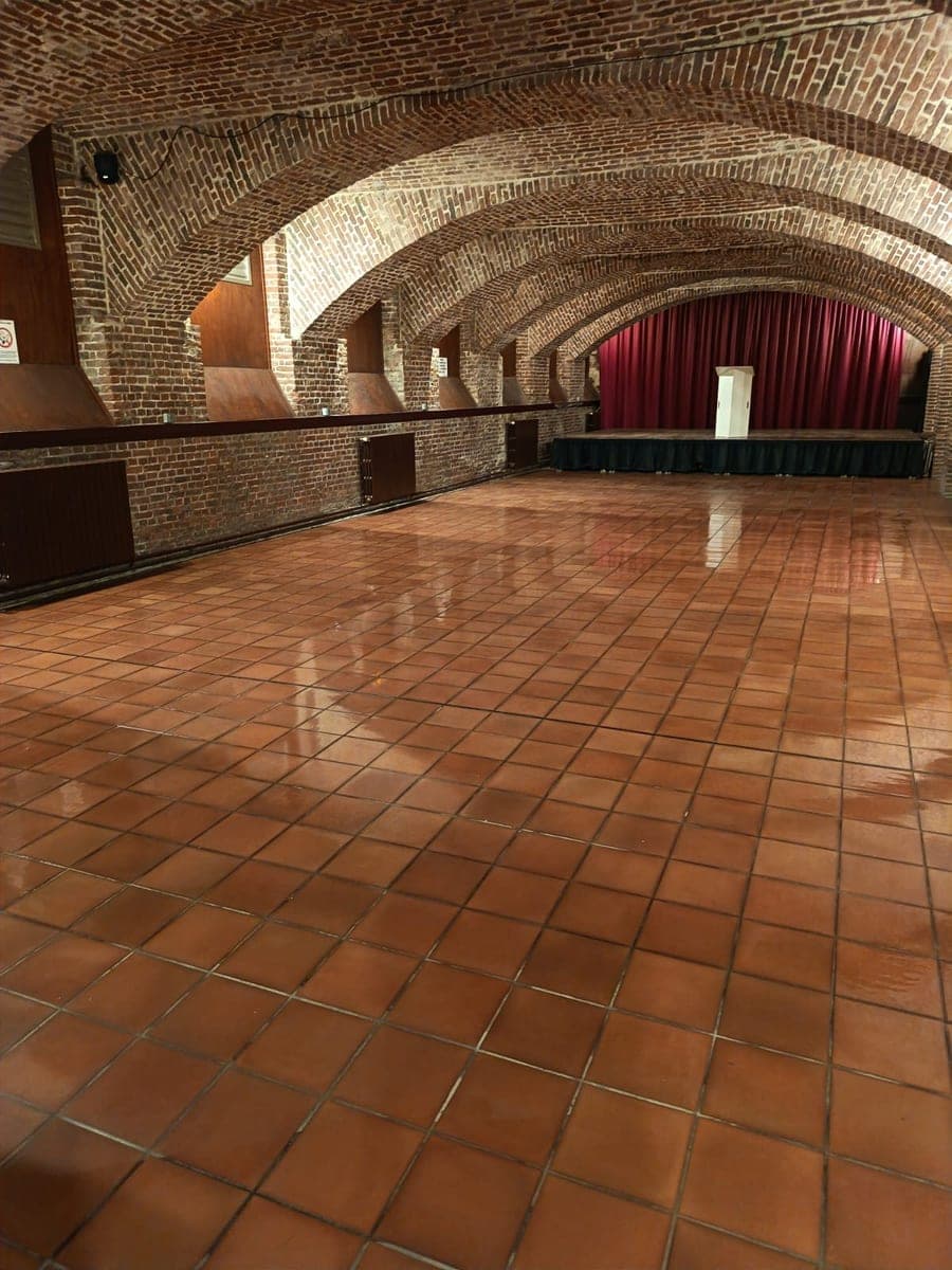 Grande salle voûtée en briques, scène au fond, sol en terre cuite lavé aux reflets brillants