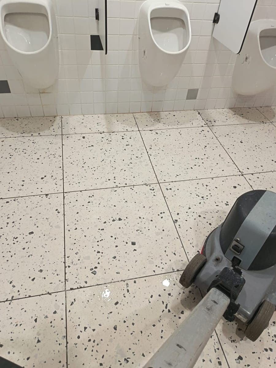 Urinoirs blancs et sol en granito mouillé, monobrosse en action sur des sanitaires de locaux