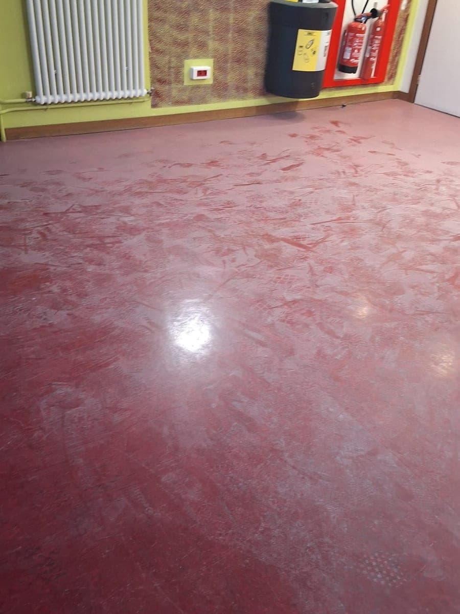 Sol rouge terne couvert d'empreintes et de traînées claires dans une salle à mur vert anis